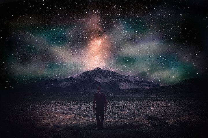 man walking through field with starlit sky